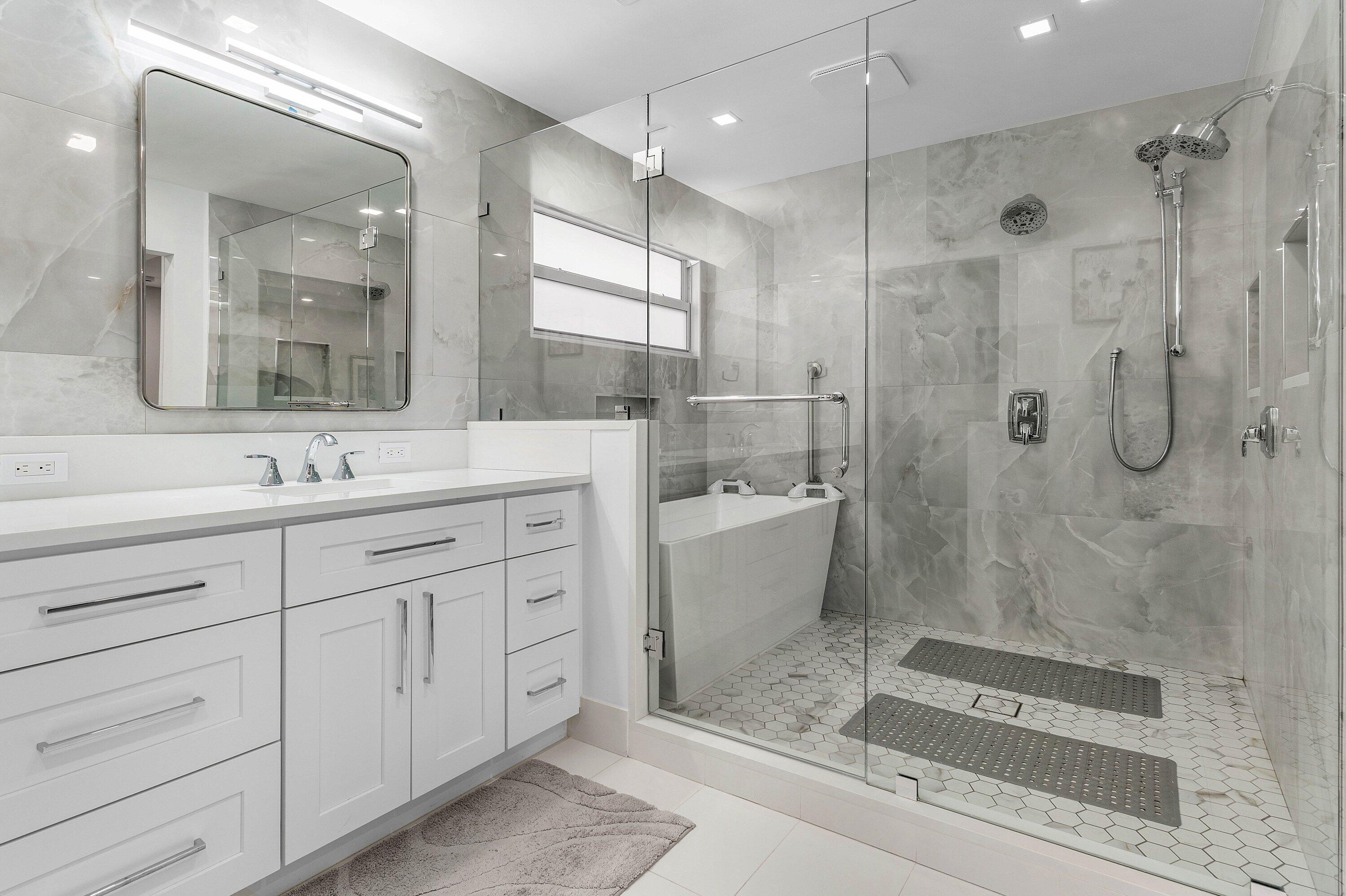 Renovated primary bathroom at 13320 Touchstone Court with frameless glass shower, freestanding tub and double vanity in grey porcelain tile